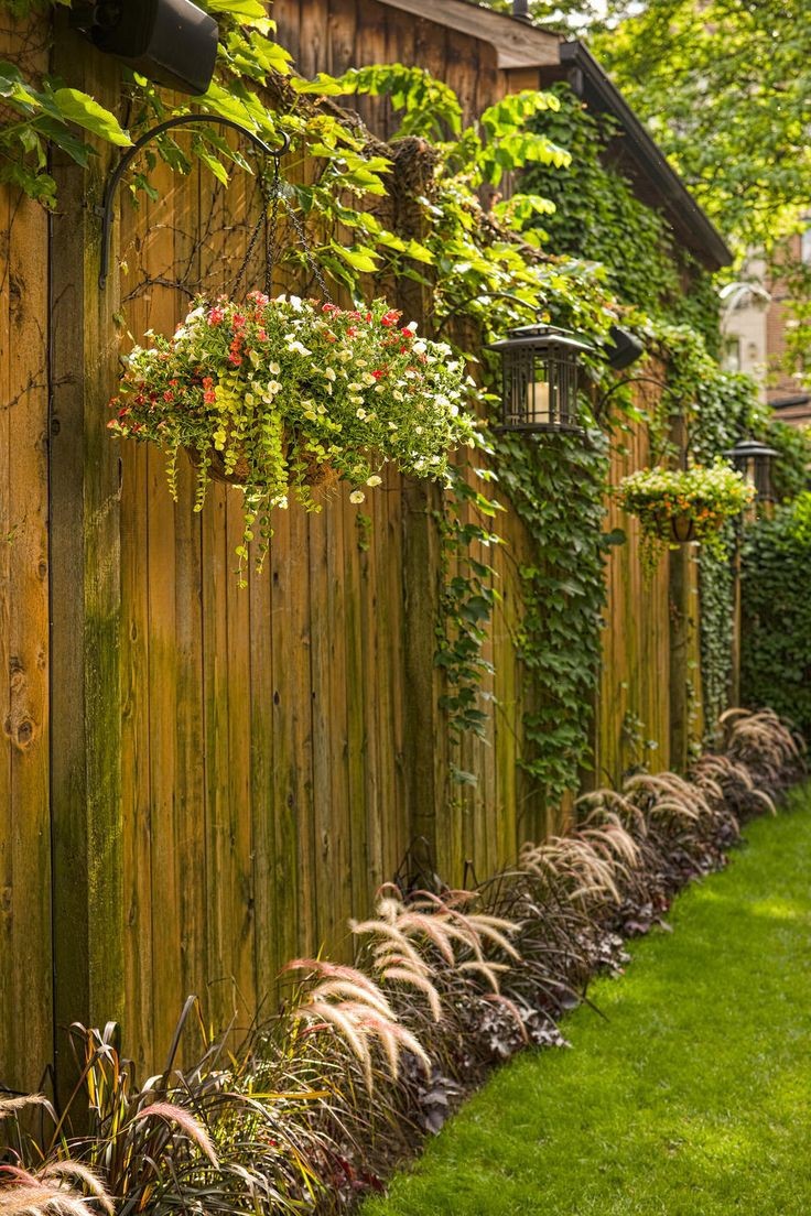 A fence decorated with hanging baskets and a flower bed